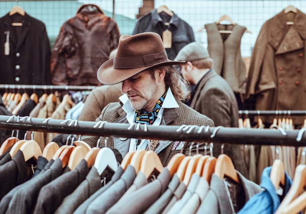 man in brown cowboy hat in front of hanged suit jackets