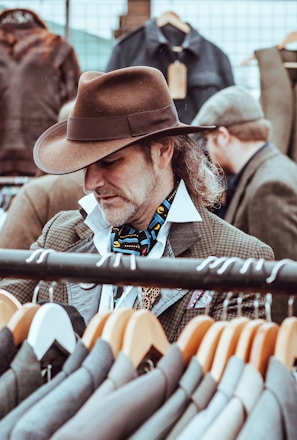 man in brown cowboy hat in front of hanged suit jackets