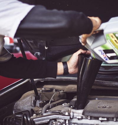 man refilling motor oil on car engine bay