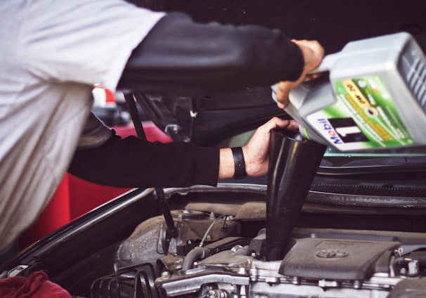 man refilling motor oil on car engine bay