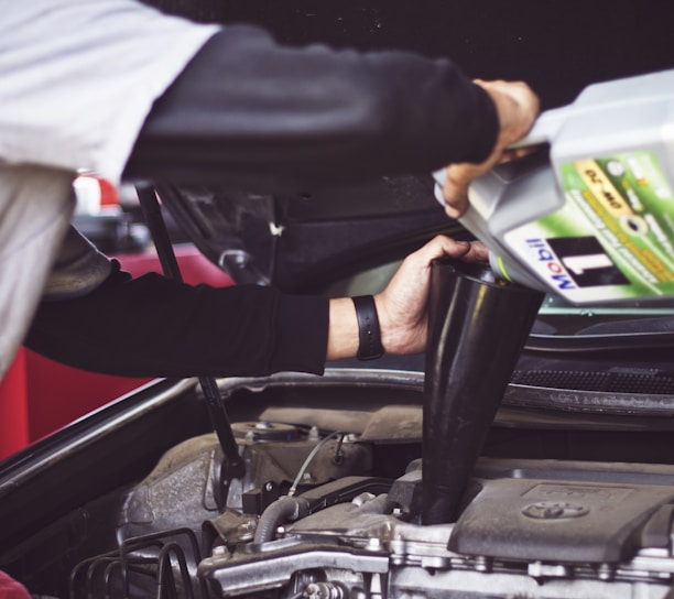 man refilling motor oil on car engine bay