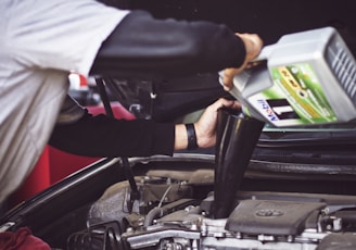 man refilling motor oil on car engine bay