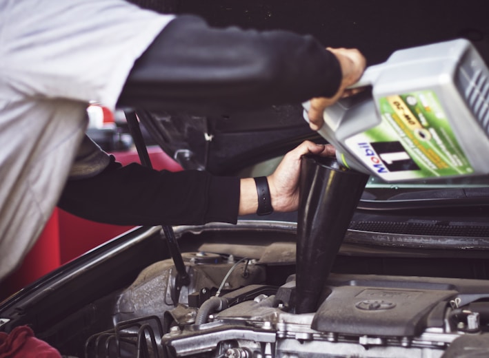 man refilling motor oil on car engine bay