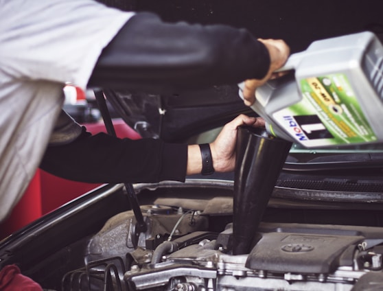 man refilling motor oil on car engine bay