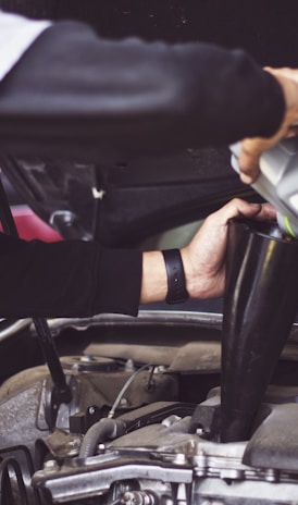 man refilling motor oil on car engine bay