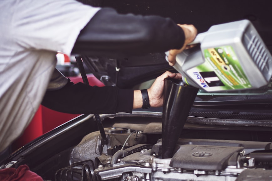 A mechanic refilling motor oil on a vehicle during an oil change.