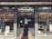 A vintage storefront for an optician, featuring weathered signage reading 'Opticians' and 'Estb 1935'. Display cases on either side showcase products like contact lenses and sunglasses, with advertisements for various eyewear brands. The building has a rustic, aged look with textured stonework surrounding the entrance.