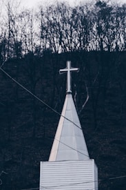 The image depicts a church steeple with a cross on top, set against a backdrop of bare trees. The scene appears to be in a dim, possibly twilight setting, with an overcast sky.
