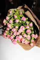 A vibrant bouquet of red and pink roses wrapped in rustic brown paper.