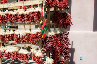 Bundles of vibrant red chili peppers drying in the sun on rustic wooden trays.