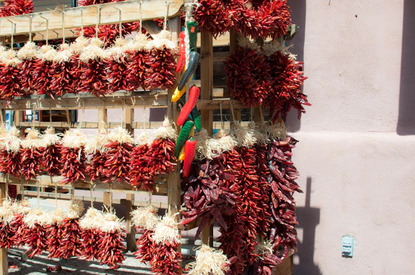 Bundles of vibrant red chili peppers drying in the sun on rustic wooden trays.