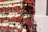 Bundles of red chili peppers are hanging on a wooden rack against a light pink wall. The chilies are intertwined with light-colored dried straw, creating a colorful and rustic display.