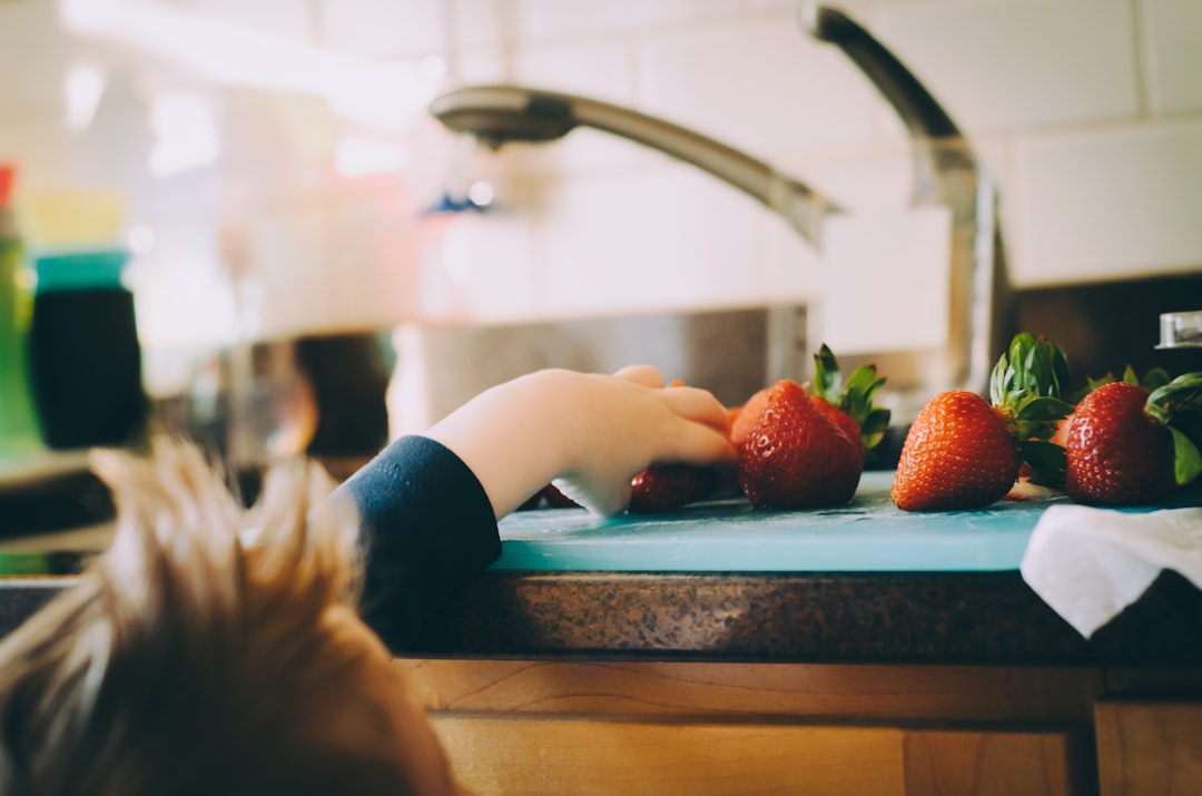 Kid reaching for fresh strawberries on the kitchen counter