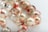 A close-up view of a strand of glossy pearls. Each pearl has a unique marbled design with shades of red, white, and subtle hints of green. The background is softly blurred, emphasizing the intricate patterns on the pearls.
