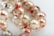 A close-up view of a strand of glossy pearls. Each pearl has a unique marbled design with shades of red, white, and subtle hints of green. The background is softly blurred, emphasizing the intricate patterns on the pearls.