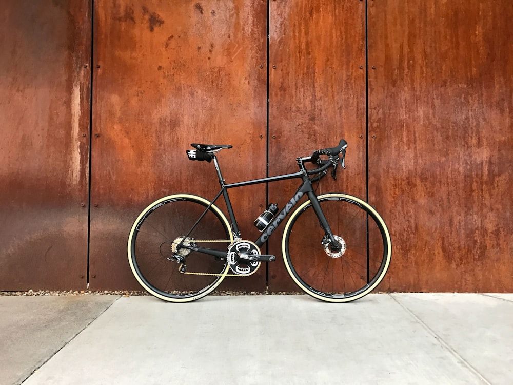 Bicicleta de carretera negra estacionada junto a una pared de madera marrón