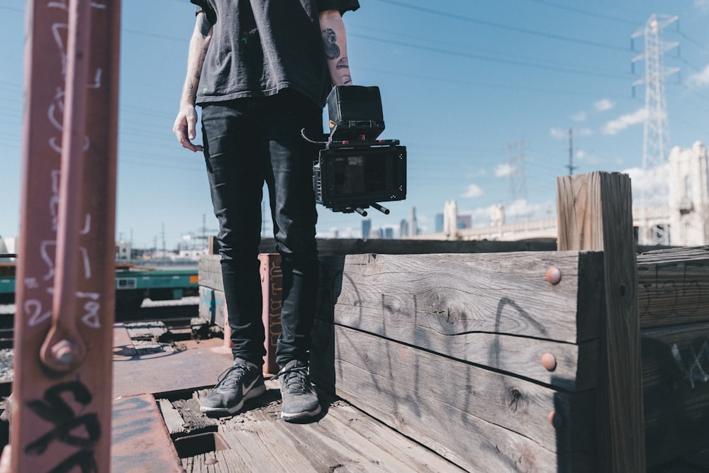 man holding black video camera while standing on plank