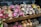 An assortment of small flower bouquets in various colors are arranged neatly on wooden shelves. The bouquets feature bright and vibrant flowers such as daisies, roses, and carnations. The display has signage with pricing details in a retail setting.