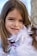 A young girl with long brown hair is smiling while adorned in a feather boa. A necklace with purple beads is around her neck, adding a playful and colorful touch.