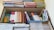 A neatly organized bookshelf containing a variety of textbooks and notebooks. The shelves are filled with academic books such as chemistry, mathematics, and physics, stacked both vertically and horizontally. There are also numerous colorful files and folders neatly arranged on the top shelf. Each section appears meticulously organized, indicating a well-maintained study space.