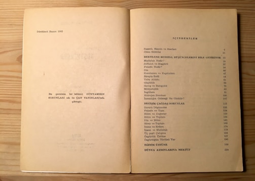 The image shows an open book on a light wood surface. The left page contains some text in Turkish, mentioning the fourth edition from 1982, and a note about the publication. The right page features a table of contents titled 'İÇİNDEKİLER', listing topics related to Bertrand Russell, philosophical and modern issues, with corresponding page numbers.