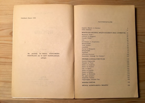 The image shows an open book on a light wood surface. The left page contains some text in Turkish, mentioning the fourth edition from 1982, and a note about the publication. The right page features a table of contents titled 'İ&Ccedil;İNDEKİLER', listing topics related to Bertrand Russell, philosophical and modern issues, with corresponding page numbers.