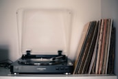 An acrylic record player stand holding a vintage turntable with vinyl records.