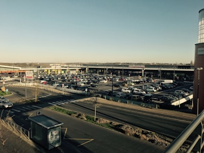 Wide shot of a busy shopping center parking area with cars and pedestrians.