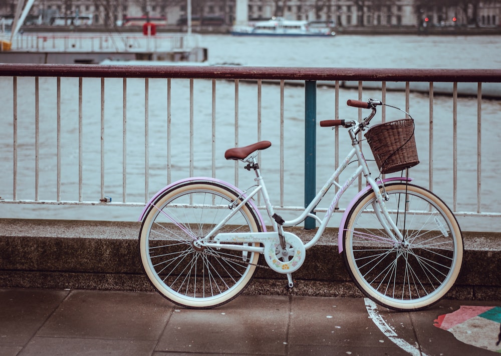 레일 근처에 주차된 바구니가 있는 흰색 도시 자전거