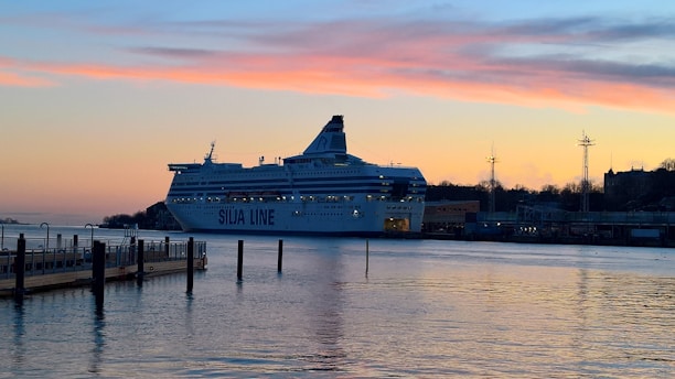 A warm-toned image showing a cruise ship docked at a bustling port during sunset.