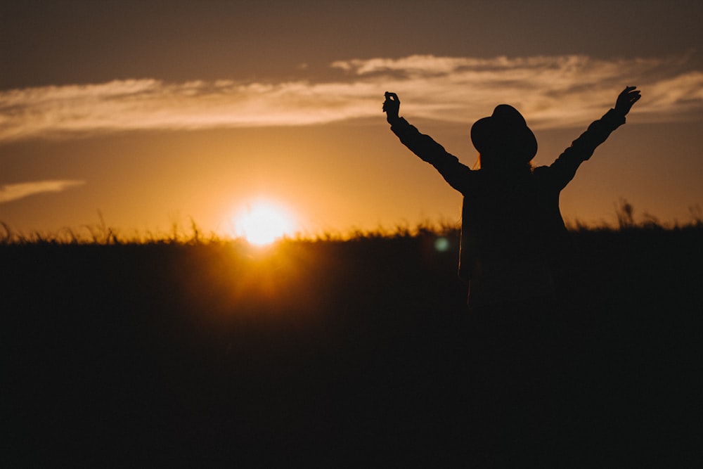 silhouette of person raising his two arms during sunrise