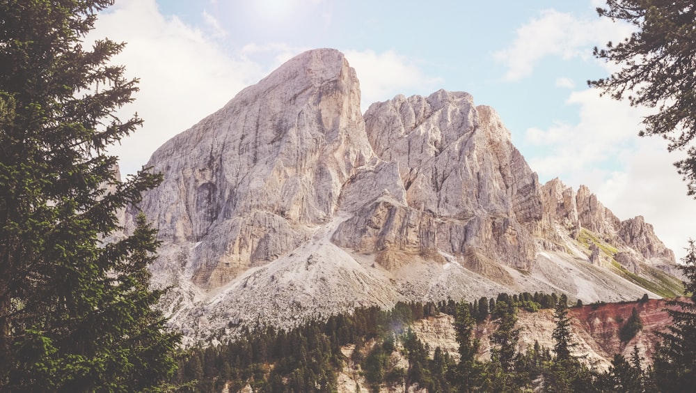 montaña marrón cerca de árboles verdes bajo cielo nublado soleado blanco y azul