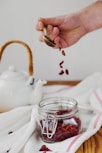person holding brown spoon above clear glass jar
