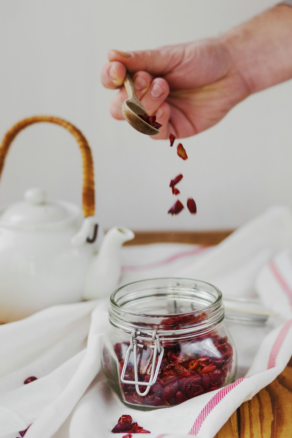 person holding brown spoon above clear glass jar