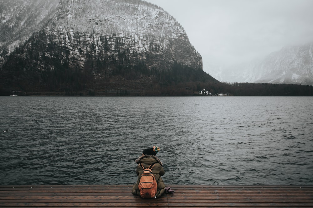 person sitting on wooden dock in front of body of water