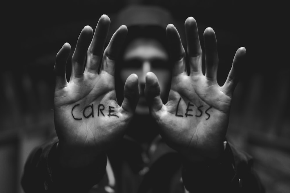 gray scale photography of man raising both hands with care less text on palm