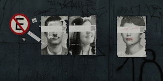 Three black-and-white portraits of people are pasted on a dark surface, each with a strip of paper or tape covering their eyes. The first and third portraits are of men, while the middle portrait is of a woman. There is a 'no parking' sign to the left and graffiti scattered around the scene.