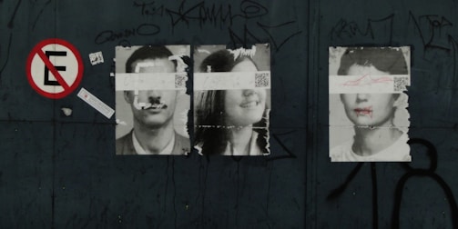 Three black-and-white portraits of people are pasted on a dark surface, each with a strip of paper or tape covering their eyes. The first and third portraits are of men, while the middle portrait is of a woman. There is a 'no parking' sign to the left and graffiti scattered around the scene.