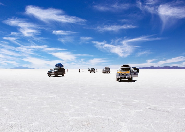 sports utility vehicles on desert under cloudy blue sky during daytime
