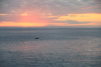 A serene pastel-colored sunrise over a calm Florida inlet with a small fishing boat gently floating.