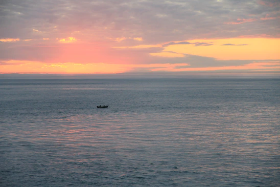 A serene ocean view at sunset with a small boat gently floating on calm waters.