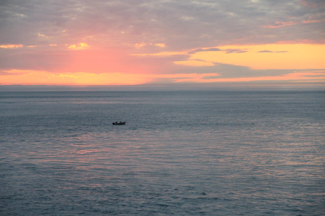 A serene pastel-colored sunrise over a calm Florida inlet with a small fishing boat gently floating.