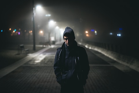 homem andando sozinho no nevoeiro à noite perto das luzes da rua