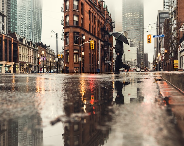 man using umbrella crossing the street during daytime