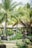 Lush tropical garden with numerous palm trees and vibrant green foliage. Traditional thatched-roof huts blend seamlessly into the natural surroundings, creating a shaded area where people gather. Intricately carved stone statues are nestled among the plants, adding a serene and cultural atmosphere.
