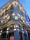 A grand, ornate building with elaborate architectural details, including columns and decorative moldings, is prominently illuminated. The structure has a luxurious appearance, enhanced by strategic lighting that highlights its features. A blue sign with the words 'Hotel Atlántico' is visible on the right side, adding to the opulent atmosphere.