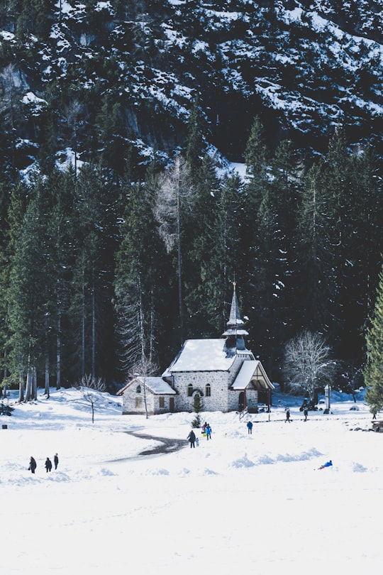 people walking on snow covered ground near white and brown house surrounded by trees during daytime in Pragser Wildsee Italy