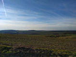 A wide open farmland bordered by modern fencing with distant hills in the background.
