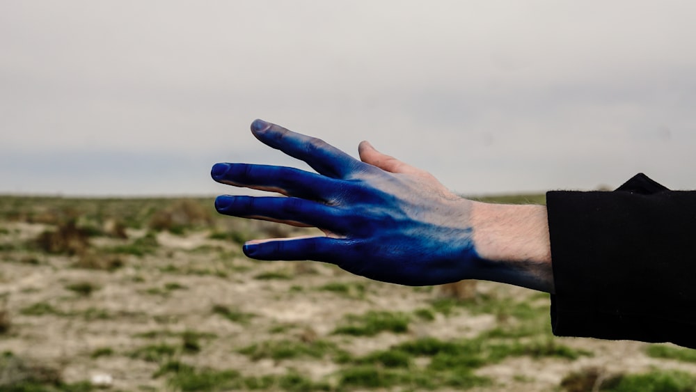 A person reaching out with their blue paint covered hand.