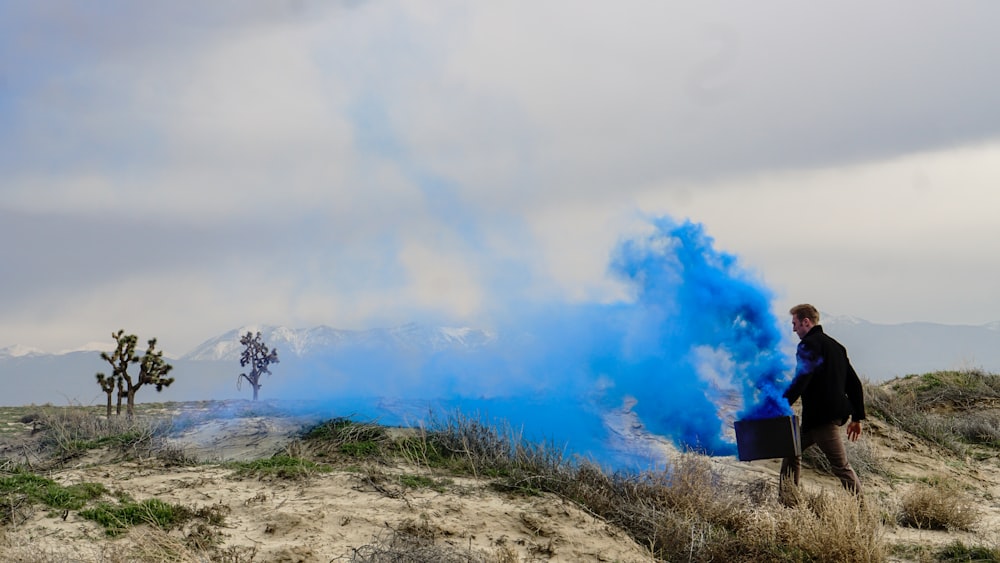 man holding black box with blue smoke walking on grass field during daytime